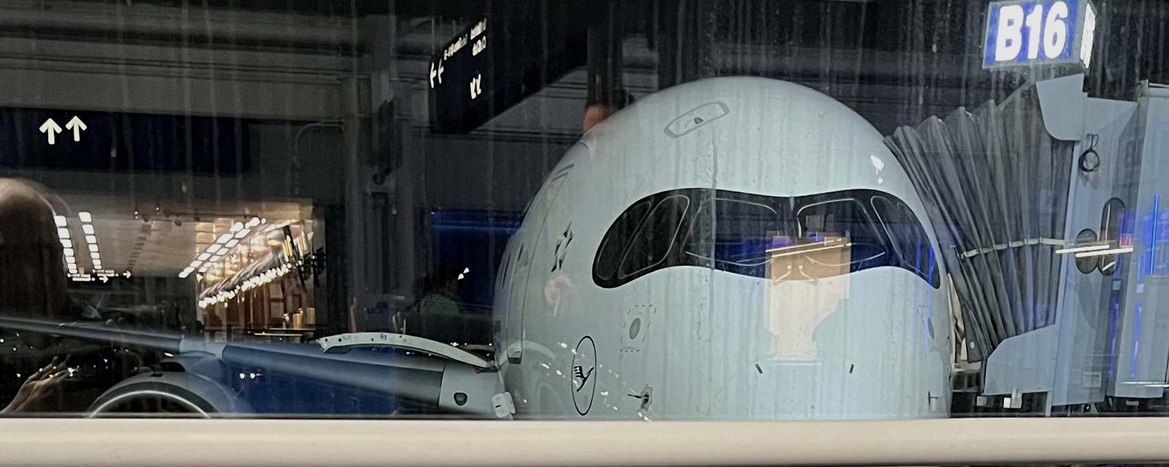Wide-body aircraft at a terminal gate at night, seen through rain-covered terminal glass.