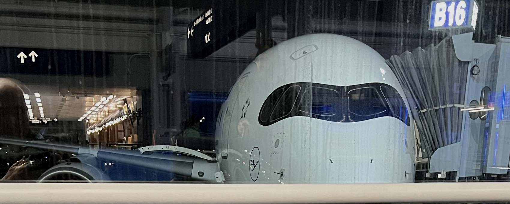 Wide-body aircraft at a terminal gate at night, seen through rain-covered terminal glass.